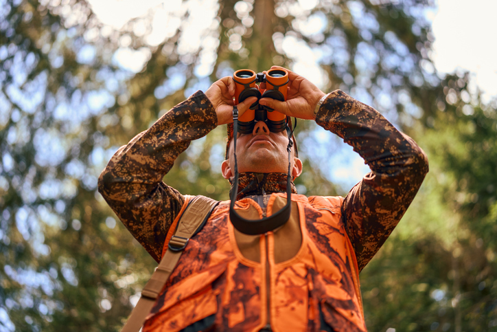 Chasseur en tenue fluo observant aux jumelles
